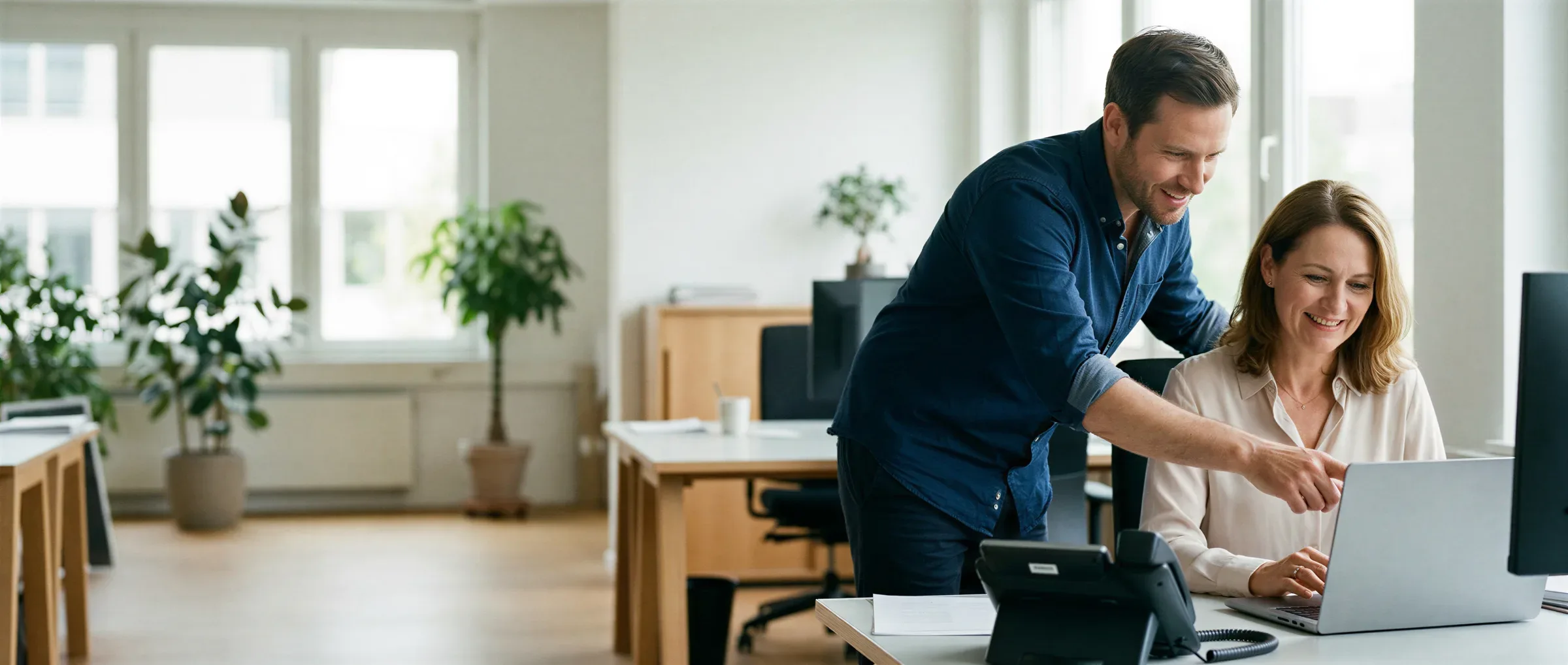 VIICO-Techniker bespricht mit einer Kundin die Telefonanlage an ihrem Arbeitsplatz, IP-Telefon auf dem Schreibtisch